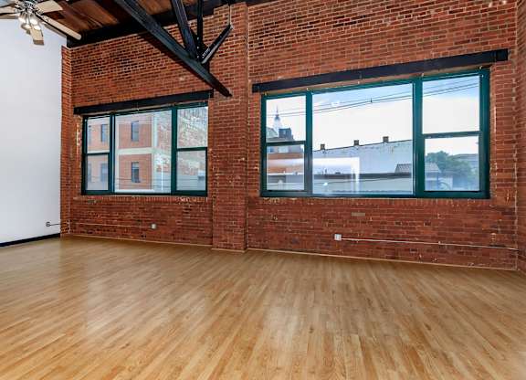 A room with wooden floors and a brick wall with windows.