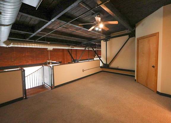 A room with a carpeted floor and a ceiling fan.