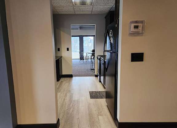 A hallway with a black fridge and a door leading to a balcony.