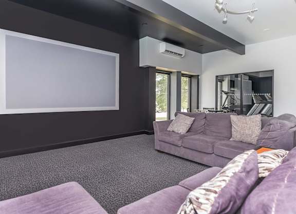 A living room with a grey couch and a large empty white screen on the wall.