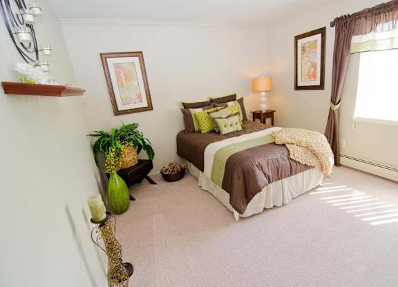 A bedroom with a bed, a plant, and a picture on the wall.