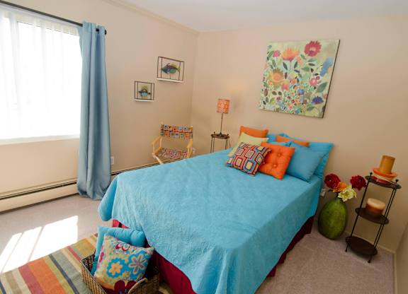 A bedroom with a blue bedspread and a basket of pillows.