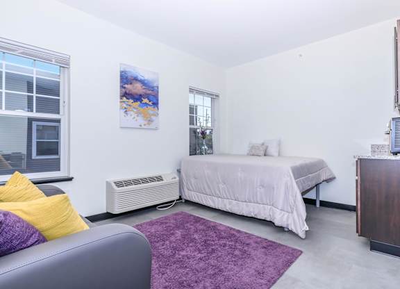 A bedroom with a bed, a couch, and a purple rug.