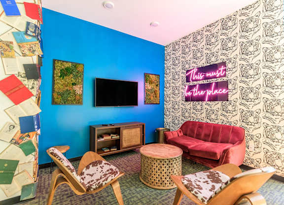 A living room with a red couch and a neon sign that says "This must be the place".