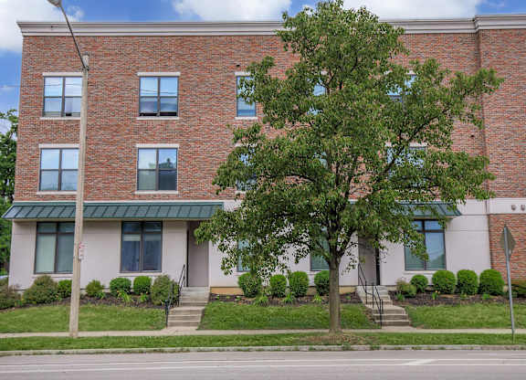A red brick building with a green roof and a tree in front.