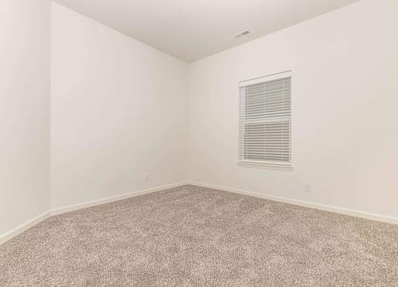 A room with a carpeted floor and a window with blinds.