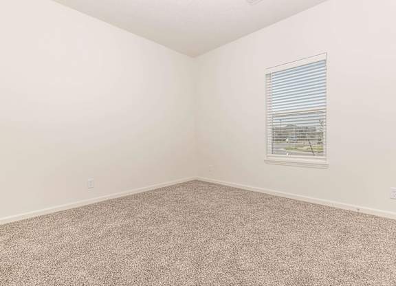 A room with a carpeted floor and a window with blinds.