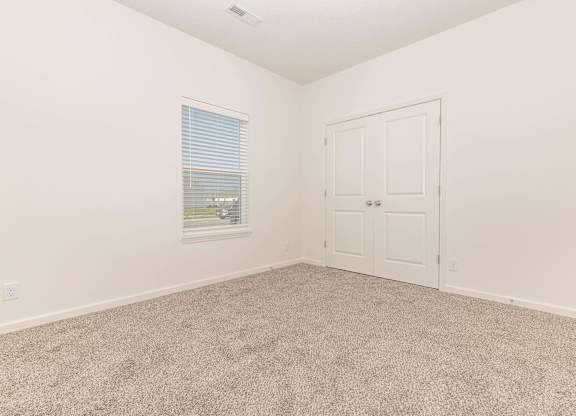 A room with a carpeted floor, a window with blinds, and a white door.