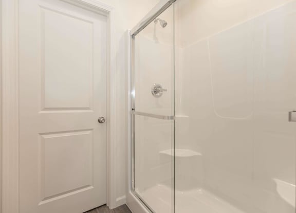 A white door is open to a glass shower stall.