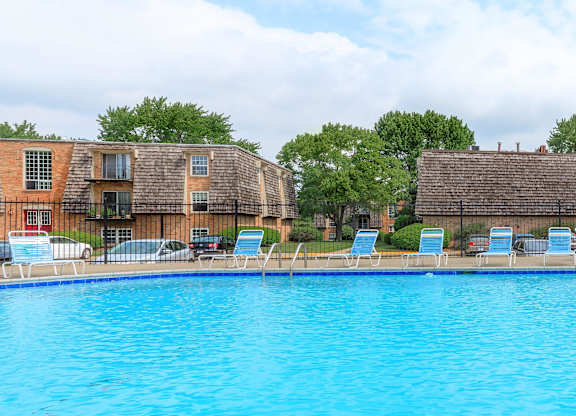 A swimming pool in front of a building with lounge chairs.