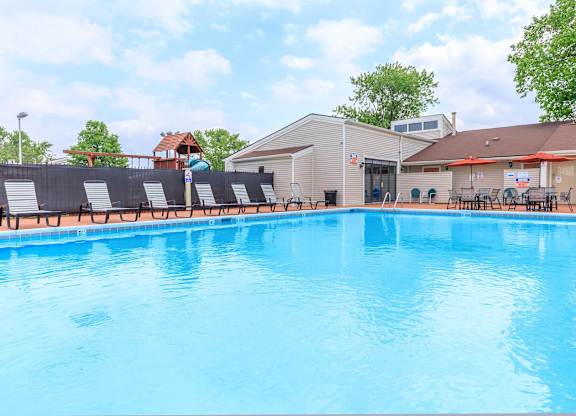 A large blue swimming pool with sun loungers and a building in the background.