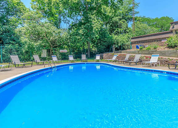 A swimming pool surrounded by trees and lounge chairs.