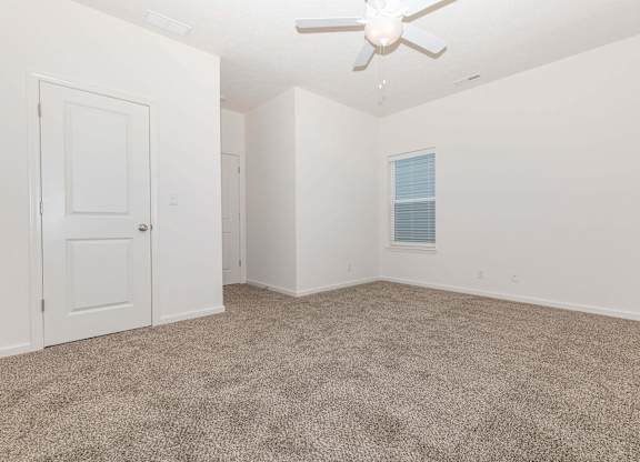 A room with a carpeted floor and a ceiling fan.