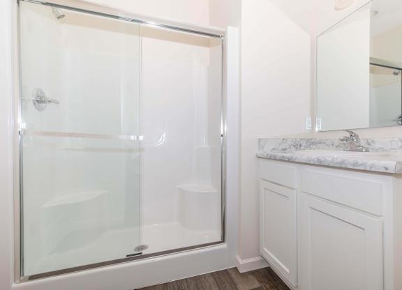 A white bathroom with a glass shower door and a marble counter.