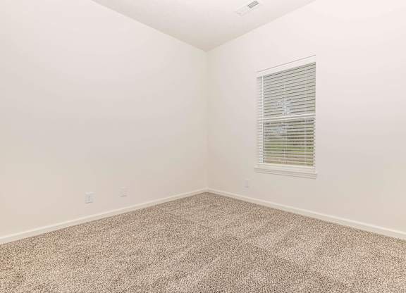 A room with a carpeted floor and a window with blinds.