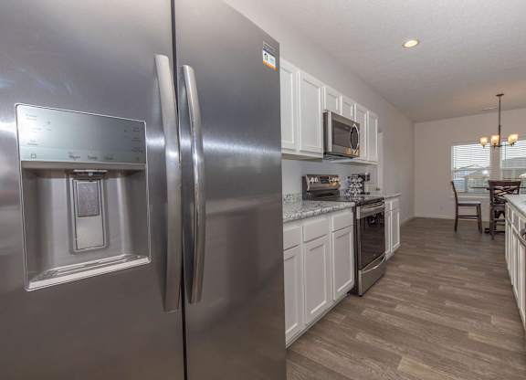 A modern kitchen with a stainless steel refrigerator and wooden flooring.