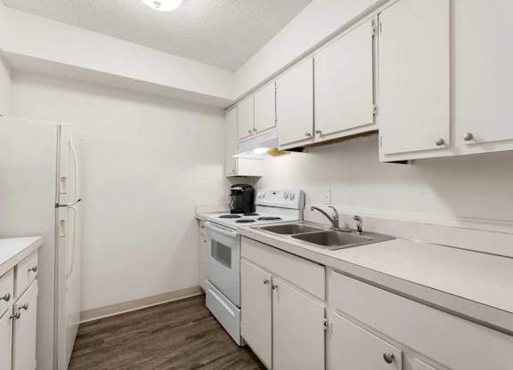 A small kitchen with white cabinets and a white fridge.