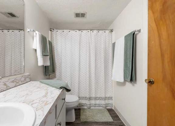 A white bathroom with a marble sink and a shower curtain.