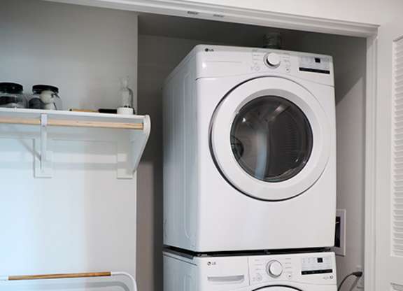 A white washing machine is stacked on top of another white washing machine in a small laundry room.