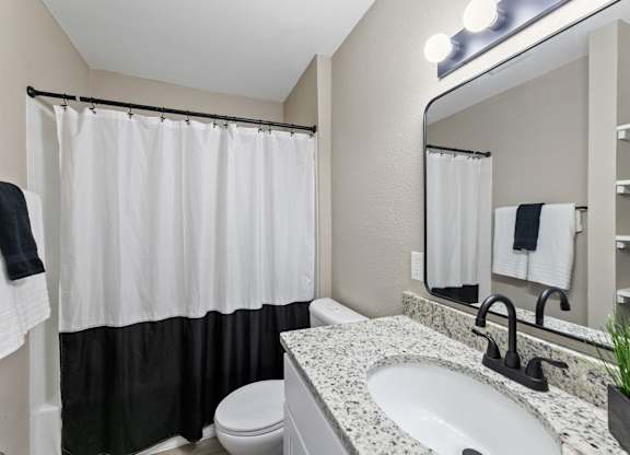 A bathroom with a white sink, toilet, and a shower with a black and white curtain.