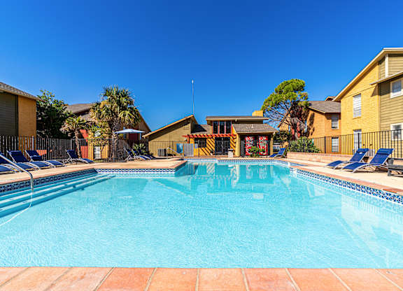 A swimming pool surrounded by lounge chairs and apartment buildings.