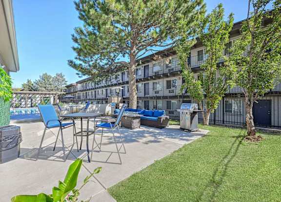 A patio with blue chairs and a table is surrounded by a fence and a tree. at Park at Fitzsimons Apartments, Aurora, MO, 80011