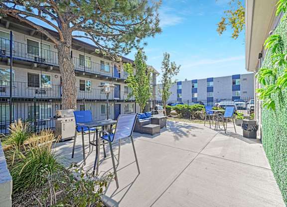 A patio with chairs and a table is surrounded by a green wall and a tree. at Park at Fitzsimons Apartments, Colorado, 80011