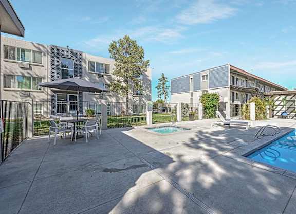 A poolside area with a table and chairs and a building in the background. at Park at Fitzsimons Apartments, Aurora, MO