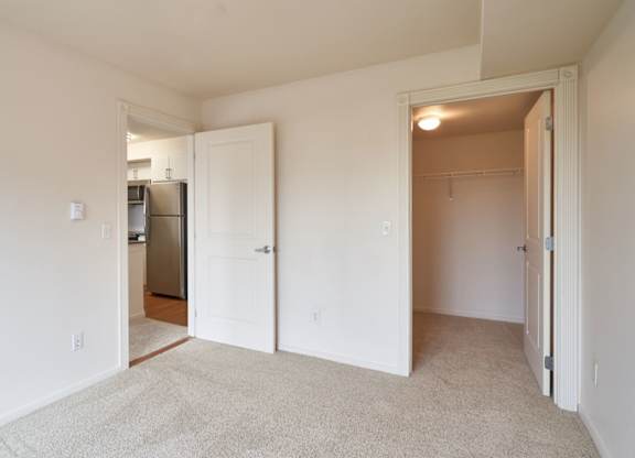 A white room with a carpeted floor and a refrigerator in the kitchen area.