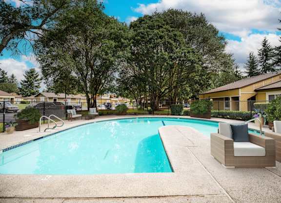 A swimming pool surrounded by trees and chairs.