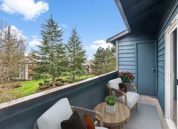 A balcony with a table and chairs overlooking a garden.