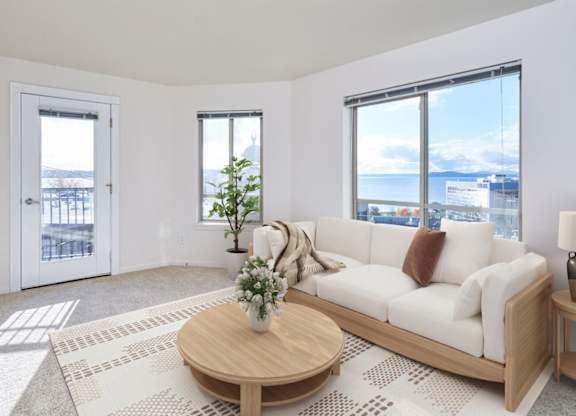 A living room with a white couch, a coffee table, and a large window overlooking the city.