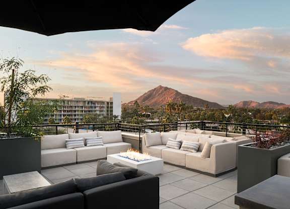 A patio with a fire pit and couches overlooks a mountain.