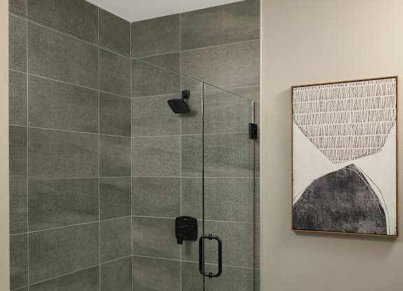 A modern bathroom with a glass shower stall and a framed artwork on the wall.