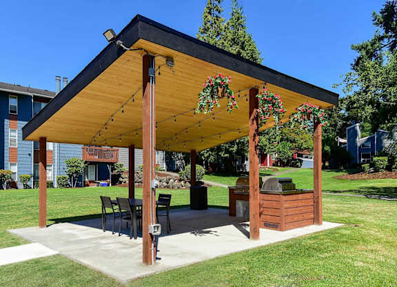 A wooden pavilion with a black roof and decorative red flowers hangs over a picnic table. at Brookstone, Washington, 98198