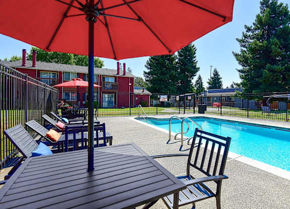 A pool area with a red umbrella and a table and chairs. at Brookstone, SeaTac, Washington