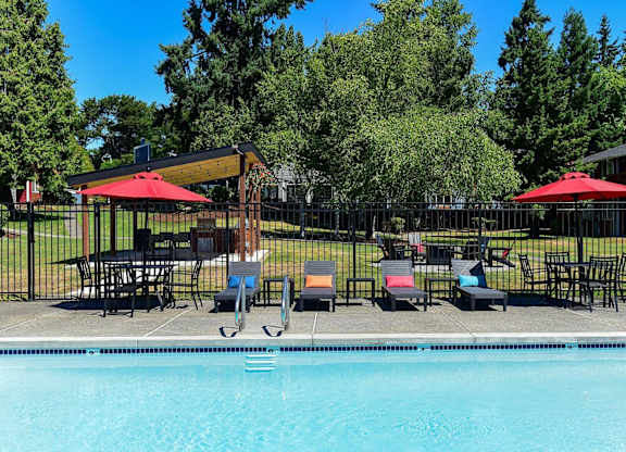 A pool with a table and chairs and umbrellas. at Brookstone, SeaTac, 98198