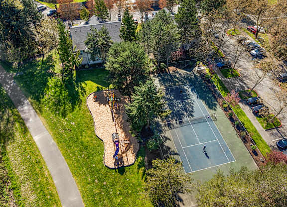 A tennis court is surrounded by trees and a playground.