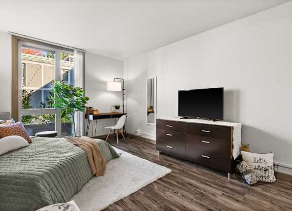 A bedroom with a bed, desk, chair, and a large window.
