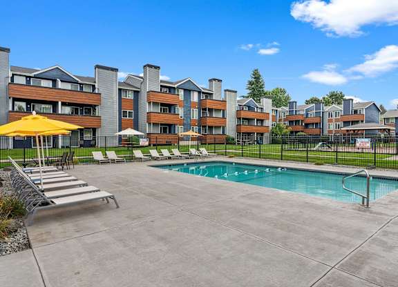 A pool area with a yellow umbrella and lounge chairs in front of a multi-story apartment building. at Northpoint Apartments, Tacoma, WA, 98407
