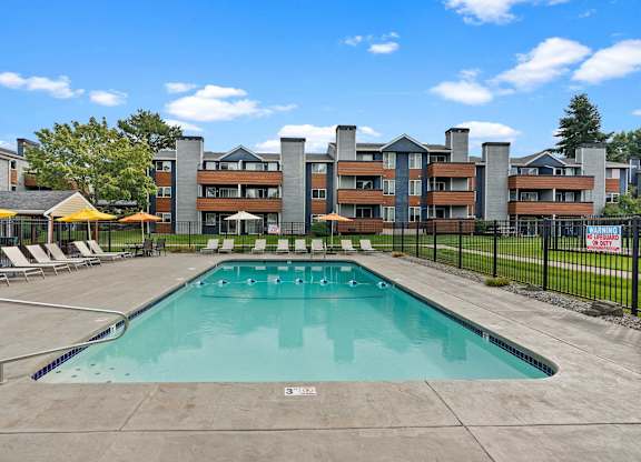 A large outdoor swimming pool with a concrete floor and a metal fence surrounding it. at Northpoint Apartments, Tacoma