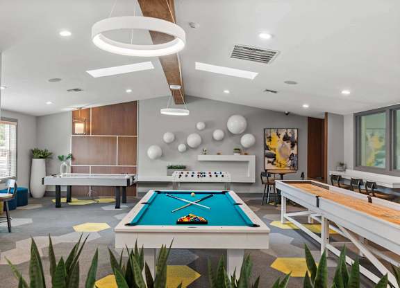 A pool table is in the middle of a room with a shelf and a painting on the wall. at Northpoint Apartments, Tacoma, WA