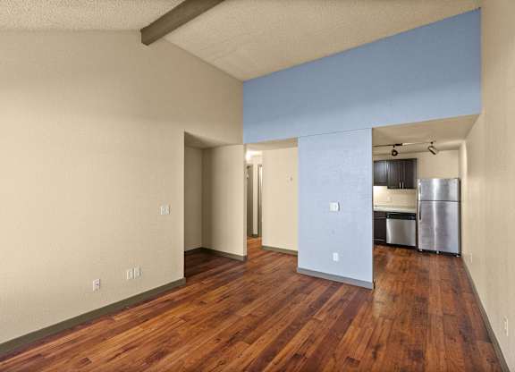 A room with wooden floors and a kitchen area in the background.