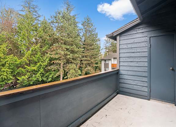 A grey deck with a door and a window overlooking a forest.