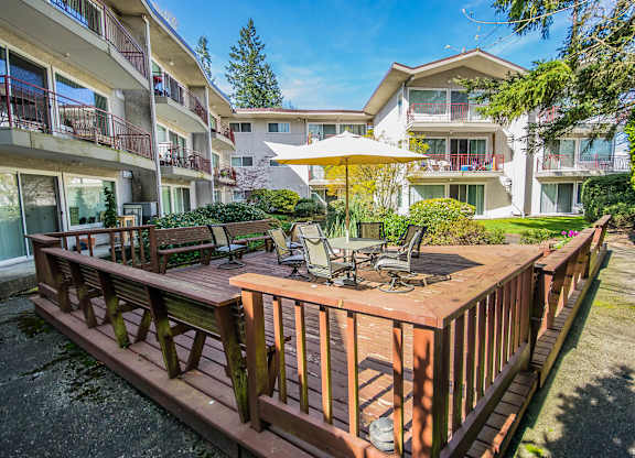 A wooden deck with chairs and a table is in the foreground of a sunny day.