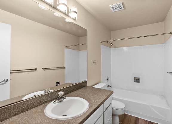 A bathroom with a sink, mirror, toilet and bathtub.