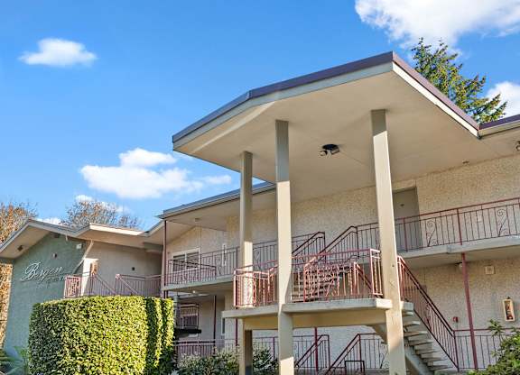 A building with a balcony and stairs is surrounded by greenery.