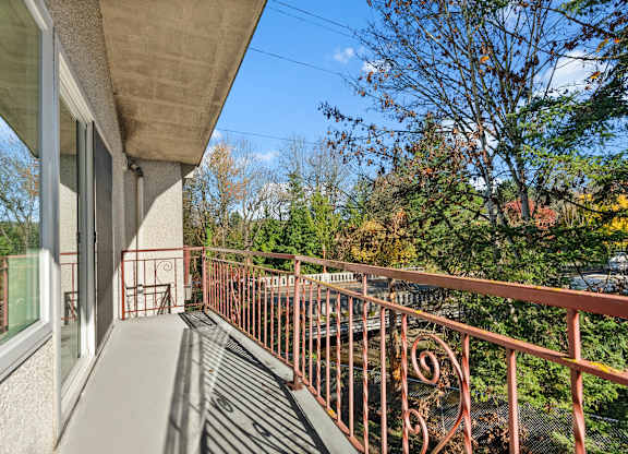 A balcony with a metal railing and a view of trees and a blue sky.