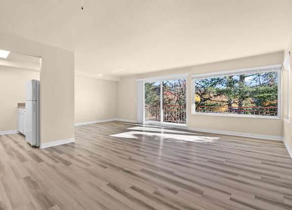 A room with wooden flooring and a large window overlooking a residential area.