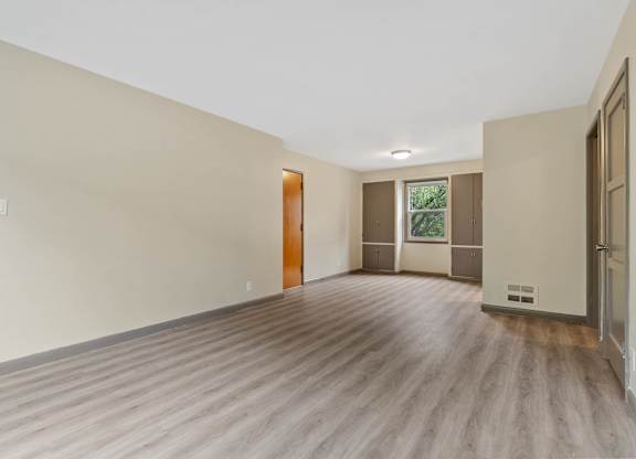 A room with wooden flooring and a window with a view of trees.
